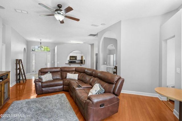 living room featuring visible vents, baseboards, light wood-type flooring, ceiling fan with notable chandelier, and arched walkways