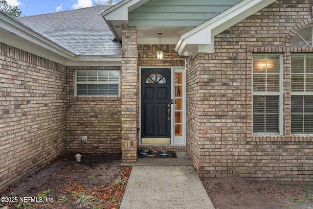 doorway to property with brick siding and roof with shingles