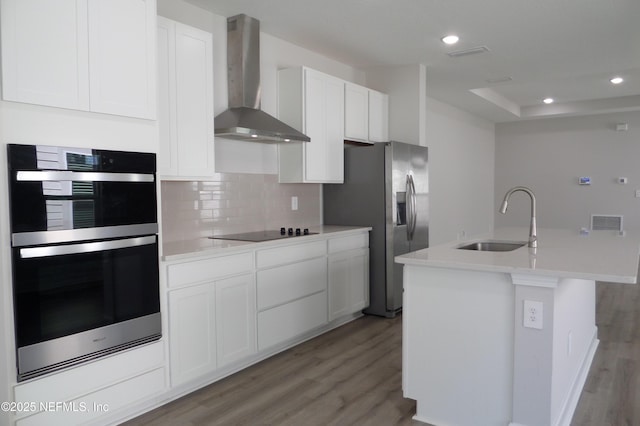 kitchen featuring a sink, appliances with stainless steel finishes, white cabinetry, wall chimney range hood, and light wood-type flooring