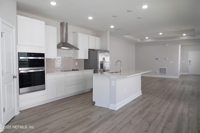 kitchen with visible vents, an island with sink, stainless steel appliances, wall chimney exhaust hood, and a sink