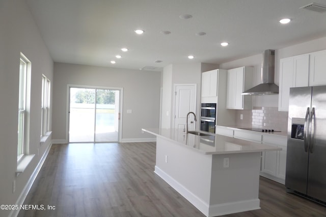 kitchen with visible vents, an island with sink, stainless steel refrigerator with ice dispenser, wall chimney range hood, and black electric stovetop