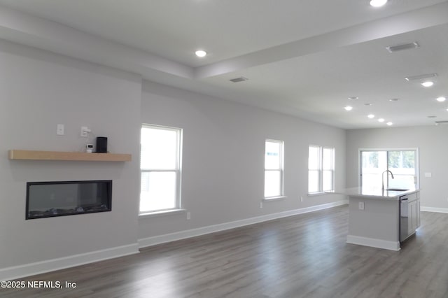 unfurnished living room with a sink, a glass covered fireplace, dark wood-style floors, recessed lighting, and baseboards