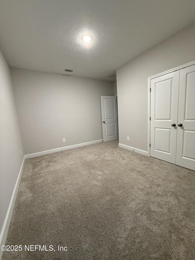 unfurnished bedroom featuring carpet, baseboards, visible vents, a closet, and a textured ceiling