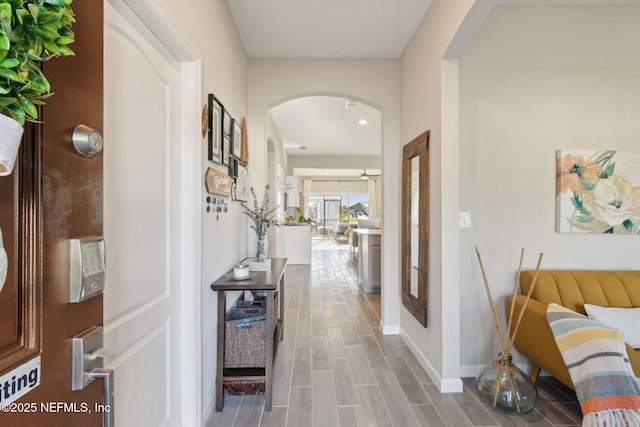 corridor with baseboards, arched walkways, and wood finish floors