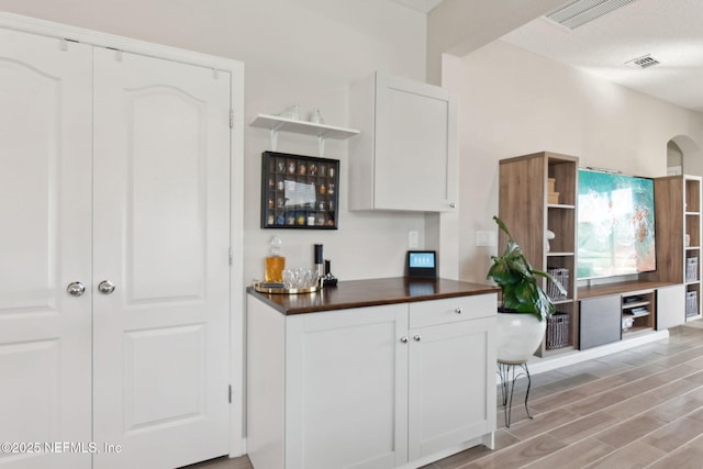 kitchen with visible vents, open shelves, dark countertops, light wood-style floors, and white cabinets