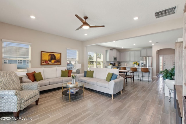 living area with a ceiling fan, visible vents, wood tiled floor, recessed lighting, and arched walkways