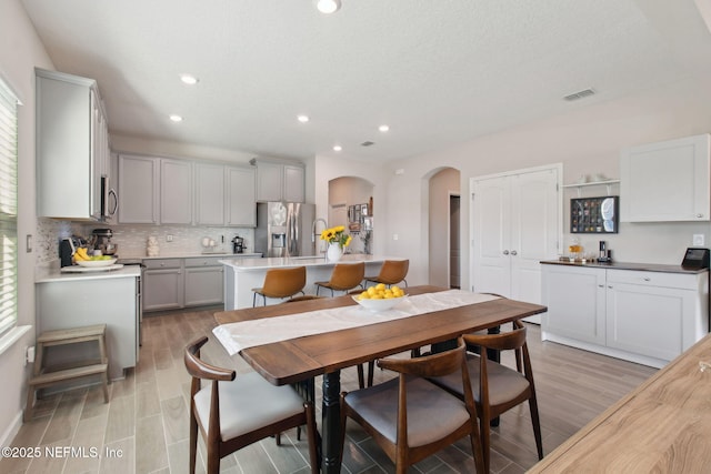 dining area with visible vents, a healthy amount of sunlight, arched walkways, and light wood finished floors