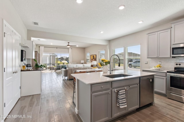 kitchen featuring visible vents, gray cabinetry, wood finish floors, appliances with stainless steel finishes, and a sink