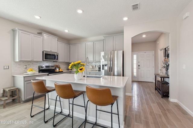 kitchen with visible vents, wood finish floors, decorative backsplash, arched walkways, and stainless steel appliances