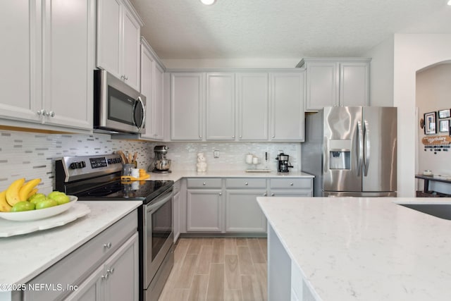 kitchen with light stone countertops, light wood-style flooring, appliances with stainless steel finishes, a textured ceiling, and tasteful backsplash