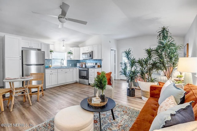 living area featuring lofted ceiling, light wood-style flooring, and a ceiling fan