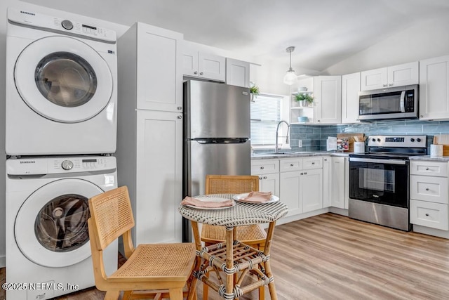 kitchen featuring stacked washer and dryer, stainless steel appliances, white cabinets, decorative backsplash, and lofted ceiling