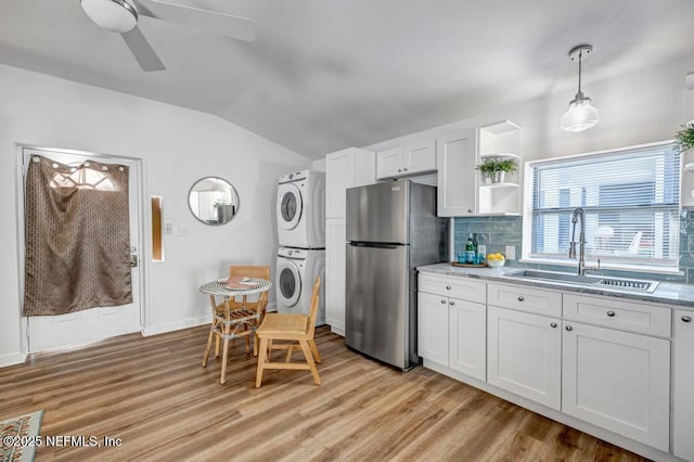 kitchen with a sink, light wood-style floors, stacked washer and clothes dryer, and freestanding refrigerator