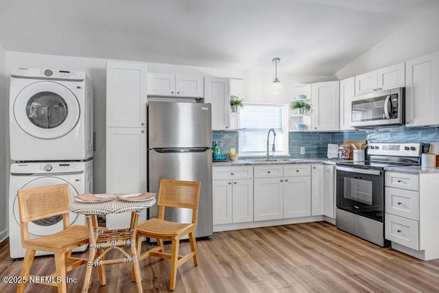 kitchen featuring lofted ceiling, a sink, white cabinets, stacked washer / drying machine, and appliances with stainless steel finishes