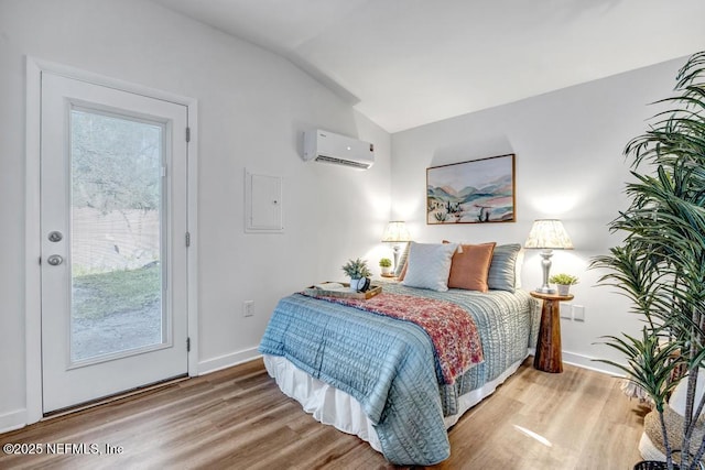 bedroom with baseboards, lofted ceiling, wood finished floors, and a wall unit AC