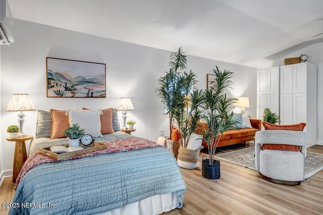 bedroom with lofted ceiling, a wall unit AC, and light wood finished floors