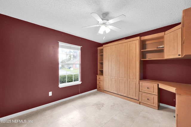 unfurnished bedroom with baseboards, a textured ceiling, ceiling fan, and built in desk