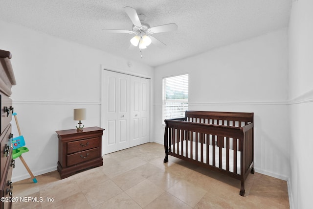 bedroom with a ceiling fan, a textured ceiling, a closet, a nursery area, and baseboards