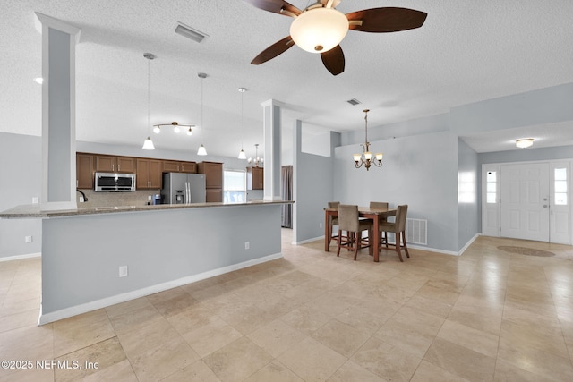 kitchen featuring visible vents, decorative light fixtures, stainless steel appliances, brown cabinetry, and a textured ceiling