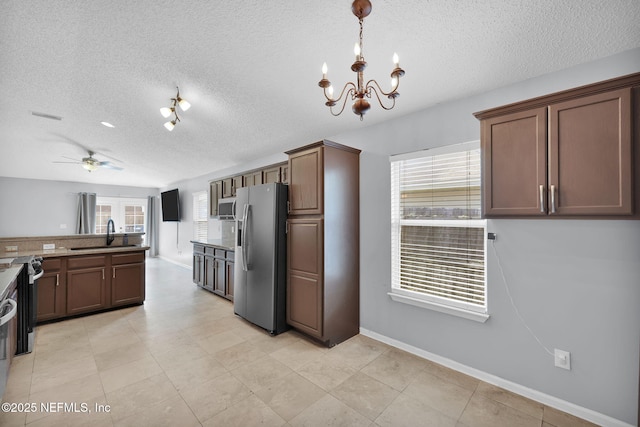 kitchen featuring ceiling fan with notable chandelier, a sink, a textured ceiling, stainless steel appliances, and baseboards