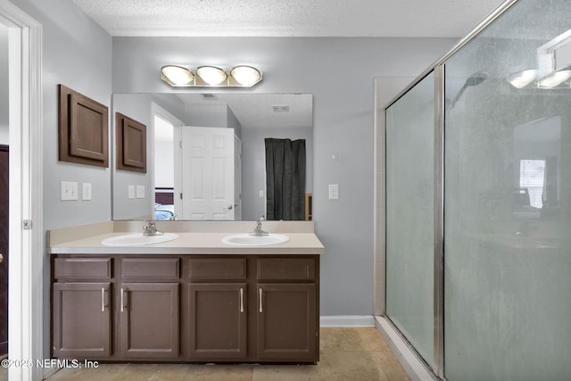 full bath featuring double vanity, a stall shower, a textured ceiling, and a sink