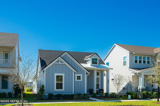 view of front of house with a standing seam roof, a shingled roof, a front lawn, board and batten siding, and metal roof