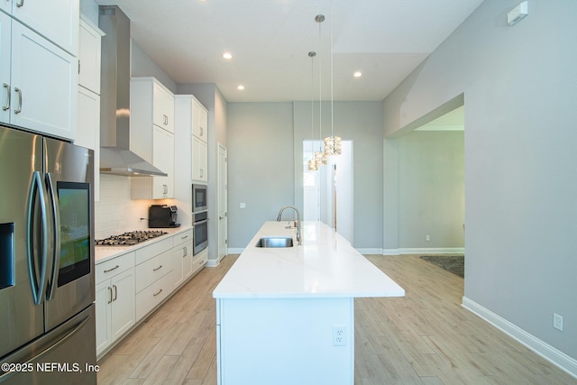 kitchen featuring wall chimney range hood, an island with sink, decorative backsplash, stainless steel appliances, and a sink