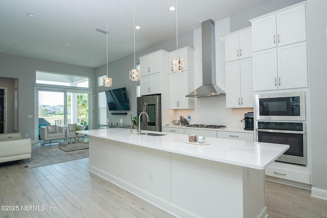 kitchen featuring visible vents, a sink, decorative backsplash, appliances with stainless steel finishes, and wall chimney range hood