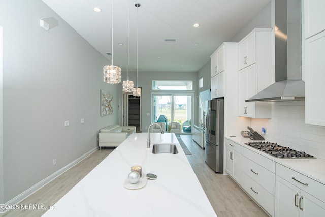 kitchen with light wood finished floors, wall chimney range hood, decorative backsplash, appliances with stainless steel finishes, and a sink