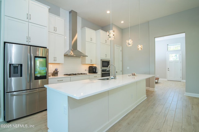 kitchen with tasteful backsplash, a sink, stainless steel appliances, wall chimney exhaust hood, and light wood-type flooring