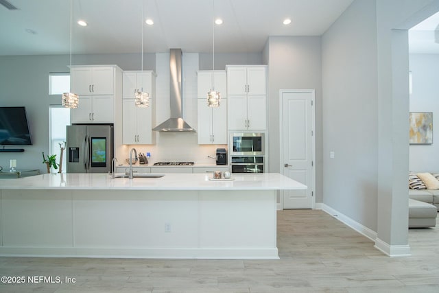 kitchen with a sink, appliances with stainless steel finishes, white cabinets, and wall chimney range hood