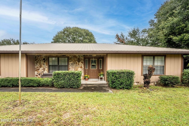 ranch-style home with metal roof, stone siding, covered porch, and a front yard