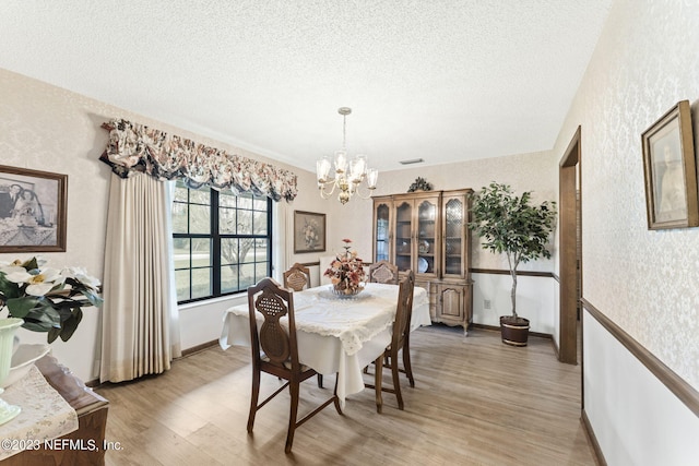 dining space featuring light wood-style flooring, a textured ceiling, wallpapered walls, baseboards, and a chandelier