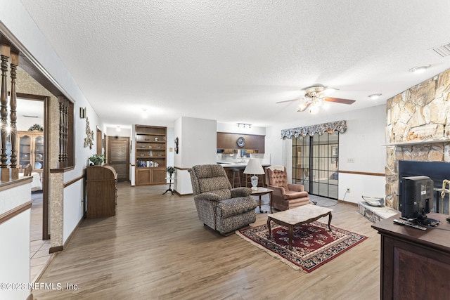 living room with light wood-type flooring, a textured ceiling, and a ceiling fan