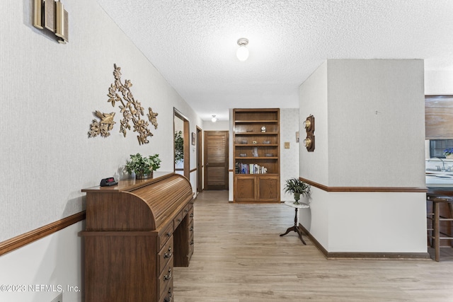 hall with a sink, light wood-type flooring, baseboards, and a textured ceiling