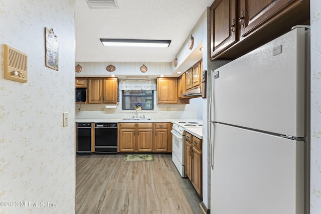 kitchen with a sink, under cabinet range hood, wallpapered walls, white appliances, and light countertops