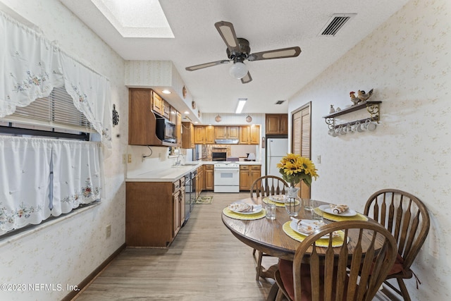 dining space with visible vents, a textured ceiling, light wood-style floors, a skylight, and wallpapered walls