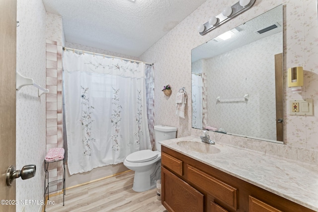 bathroom with wallpapered walls, toilet, vanity, wood finished floors, and a textured ceiling