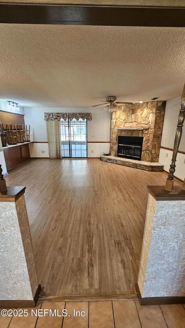 unfurnished living room with ceiling fan, wood finished floors, a fireplace, and a textured ceiling