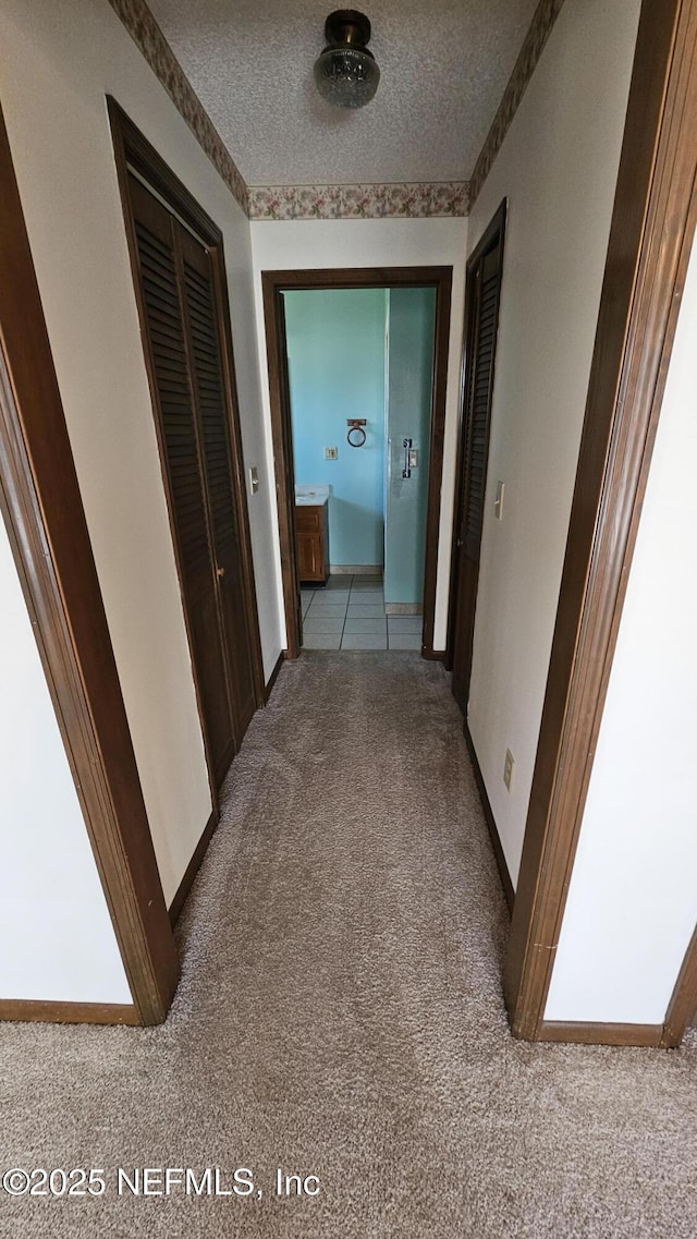 hallway featuring light colored carpet, baseboards, and a textured ceiling