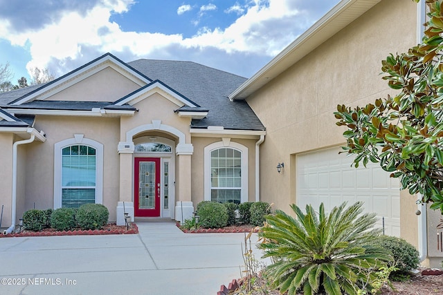 entrance to property featuring a shingled roof, an attached garage, and stucco siding