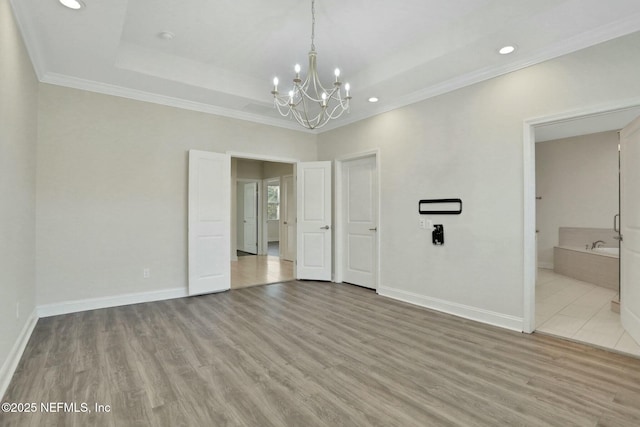 interior space with wood finished floors, baseboards, a tray ceiling, ornamental molding, and a notable chandelier