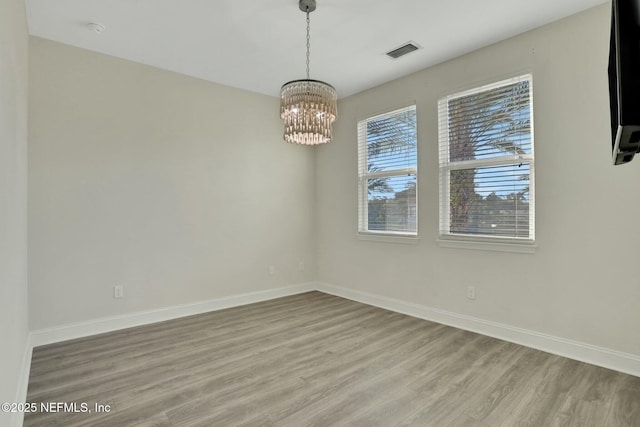 unfurnished room featuring visible vents, baseboards, light wood-type flooring, and an inviting chandelier