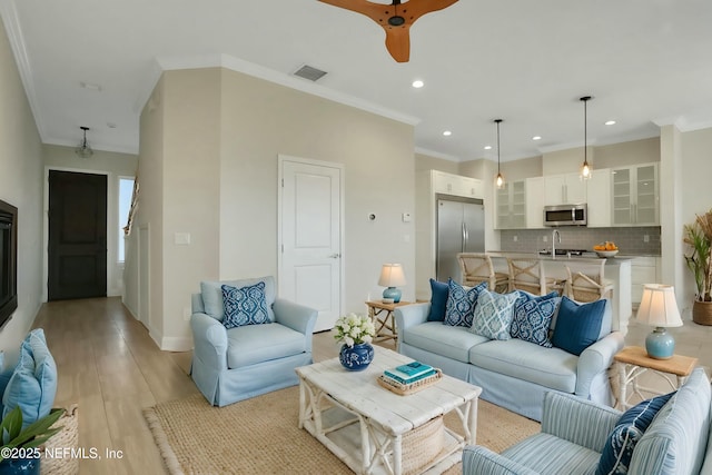 living room featuring light wood-style flooring, a ceiling fan, visible vents, and ornamental molding