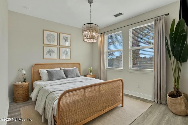 bedroom featuring visible vents, baseboards, a notable chandelier, and light wood-style flooring