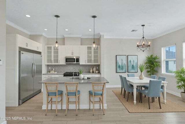 kitchen featuring visible vents, a center island with sink, backsplash, stainless steel appliances, and a chandelier