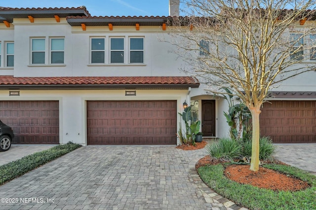 townhome / multi-family property with decorative driveway, stucco siding, an attached garage, and a tile roof