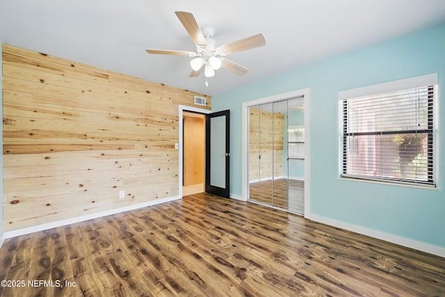 unfurnished bedroom featuring wood finished floors, visible vents, baseboards, a closet, and wood walls