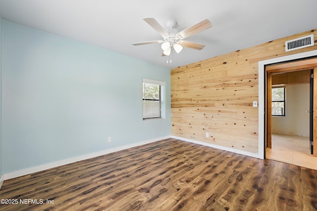 unfurnished room with visible vents, wood finished floors, plenty of natural light, and wood walls