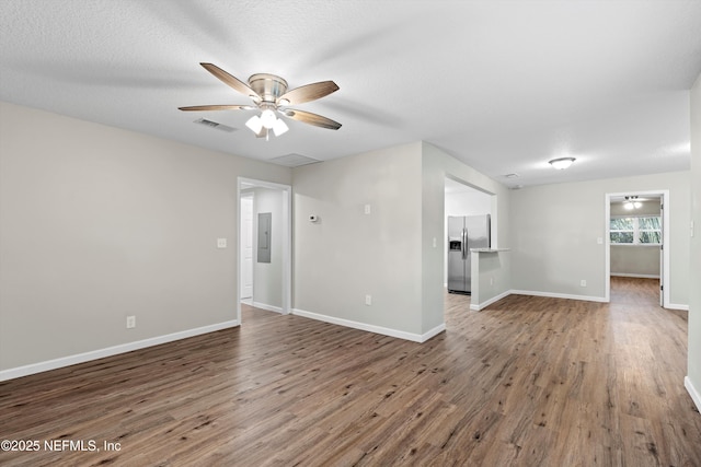 unfurnished living room with electric panel, visible vents, baseboards, and wood finished floors